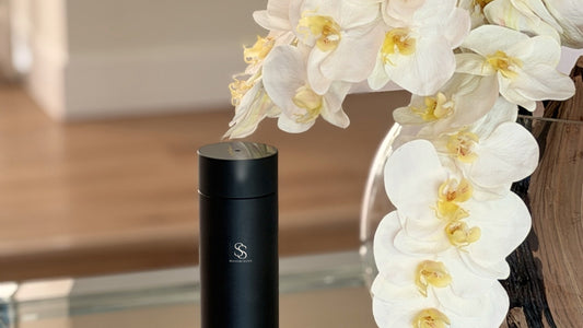 Signature Scents Tower Diffuser running on a glass console table beside white orchids